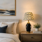 Bild in Gallery-Viewer laden, Matte black floral table lamp glowing on a bedroom nightstand