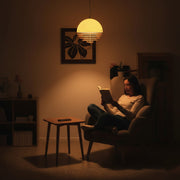  A person immersed in focused reading beneath the warm, intimate glow of the Sunset Pendant Light, mobile phone set aside, embodies a moment of pure relaxation free from technological intrusion.