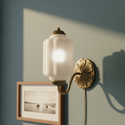 Close up of a vintage cream milk glass sconce with brass details on a sage green wall.