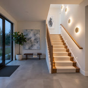 A modern home hallway and staircase lit with warm LED handrail lights and decorative wall sconces.