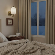 A cozy winter bedroom featuring a vintage milk glass sconce and chunky knit blankets.