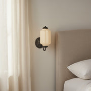 Monulo Eloise cream vintage milk glass sconce installed next to a bed with linen bedding.