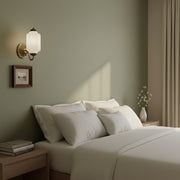 Asymmetrical bedroom decor featuring a single cream vintage milk glass sconce on one side of the bed.