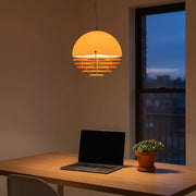 A modern home office featuring the Bauhaus Sunset Pendant Light casting a warm golden glow over a wooden desk and laptop.