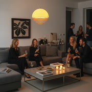 A cozy home party scene illuminated by warm sunset-style pendant lighting with guests socializing in the background.