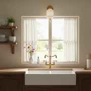 A vintage milk glass sconce with brass finish installed above a kitchen sink window in a farmhouse style kitchen.