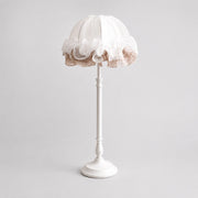 Front view of pure white ruffled fabric table lamp with sculpted metal stem