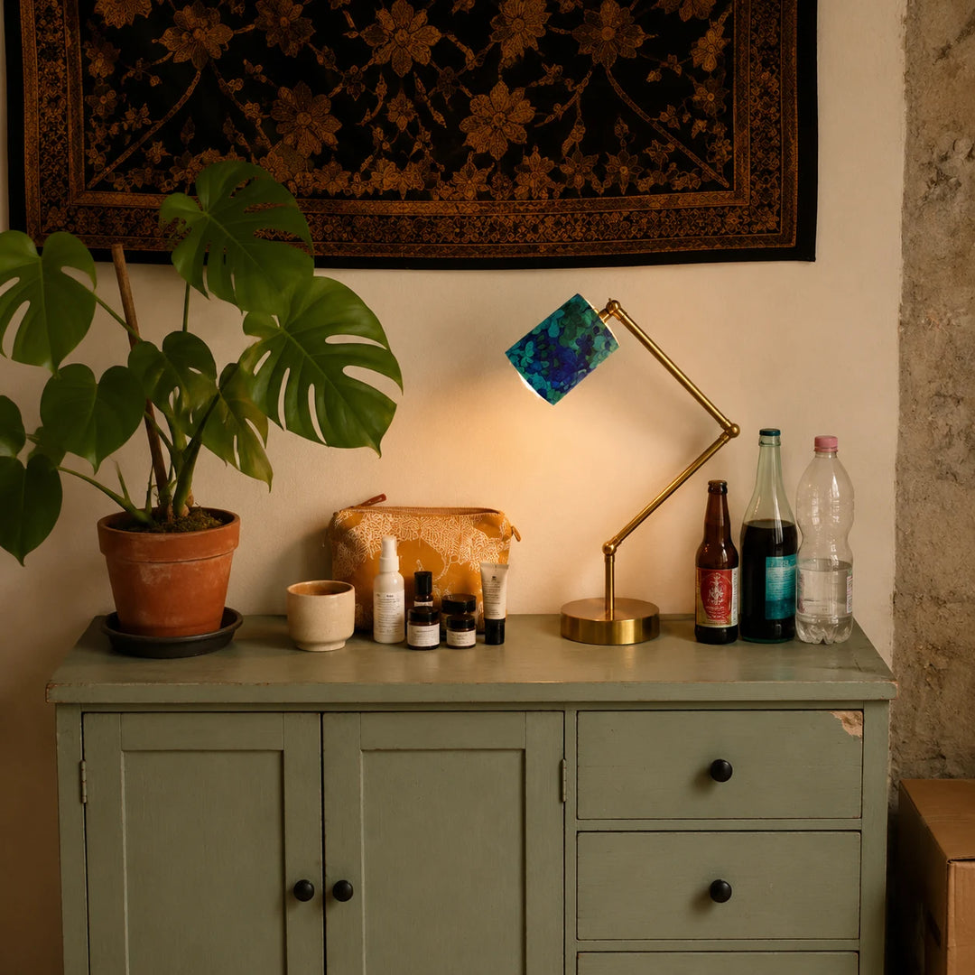 Blue green floral table lamp lit on a console with plants and decor