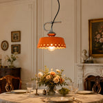 Load image into Gallery viewer, Orange metal and ceramic pendant lamp glowing over a classic dining setting