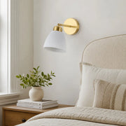 Ceramic and brass wall sconce beside a bright bedroom window