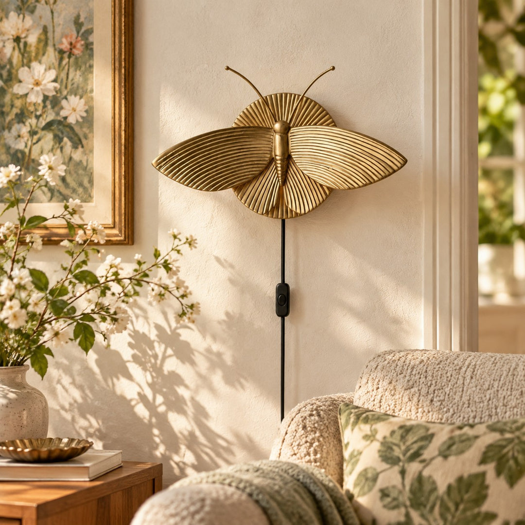 Gold moth wall sconce beside a sofa and floral artwork