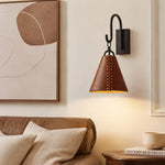 Cargar imagen en el visor de la Galería, Leather cone wall sconce casting warm light beside a bed and framed wall art