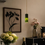 Load image into Gallery viewer, Single green jade cylinder pendant light glowing beside framed botanical wall art and flowers