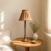 Warm tan pleated table lamp beside window in soft home corner