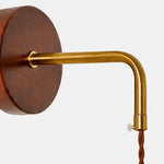 Charger l'image dans la visionneuse de galerie, Close view of the round wooden wall plate and brass arm connection on the bedside wall lamp