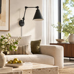 Load image into Gallery viewer, Black swing-arm sconce above a sofa in daylight