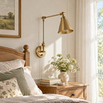 Load image into Gallery viewer, Gold swing-arm sconce beside a bed in daylight