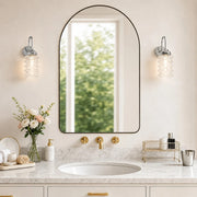 Pair of chrome ribbed glass wall sconces around an arched bathroom mirror