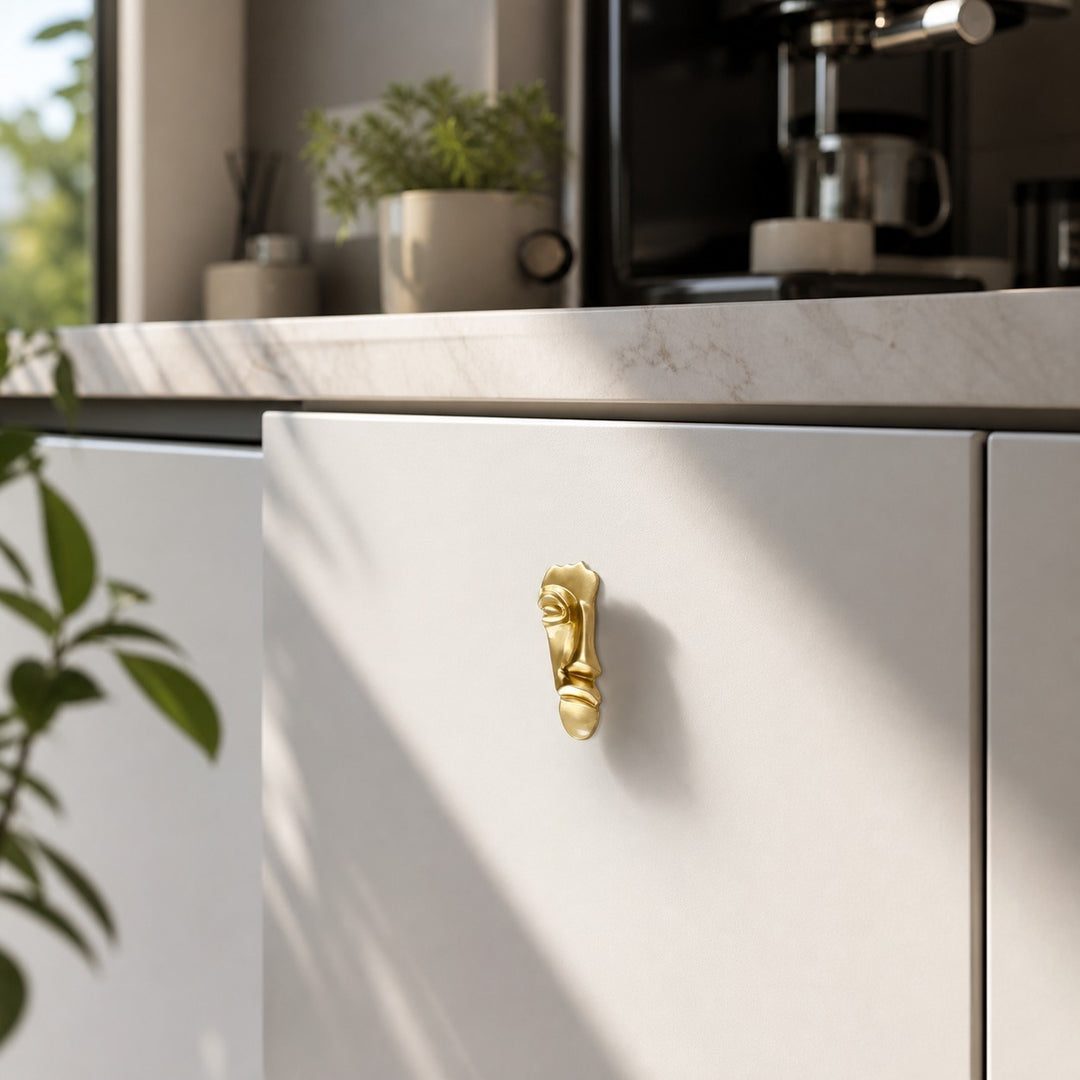 Abstract brass face cabinet knob on white kitchen cabinetry